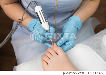 Pedicure expert performs a hardware pedicure on a woman, employing a nail drill 114517372