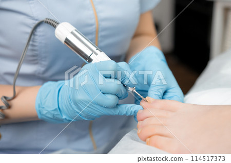 A master pedicurist provides a hardware pedicure to a woman, using a nail drill 114517373