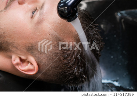 Hairdresser washes man hair from shampoo with warm water in barbershop closeup. Barber takes care of male client hair in professional salon Hairdresser washes man hair from shampoo with warm water in barbershop closeup. Barber takes care of male client hair in professional salon 114517399