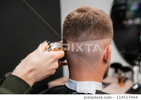 Hairstylist shaves male occiput with trimmer in barbershop closeup. Professional barber cuts man hair with machine tool in hairdressing salon Hairstylist shaves male occiput with trimmer in barbershop closeup. Professional barber cuts man hair with machine tool in hairdressing salon 114517444