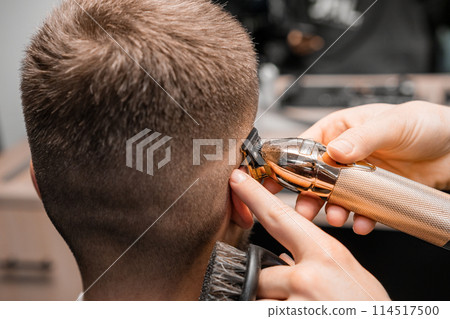 Barber shaves male client hair with trimmer in barbershop. Hairdresser shaving a mans temple Barber shaves male client hair with trimmer in barbershop. Hairdresser shaving a mans temple 114517500