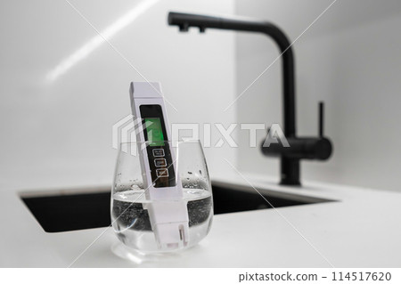 TDS meter immersed into the water in glass shows that the water is clean in modern kitchen. Clean tap water concept.  114517620