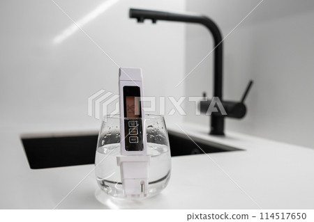 Conductometer or TDS water quality meter is immersed in a beaker of water to check purity in front of modern kitchen water tap. Dirthy water concept 114517650
