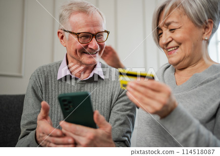 Senior couple man woman shopping online with smartphone paying with credit card. Old people buying on Internet enter credit card details at home indoors. Online shopping delivery service ecommerce 114518087
