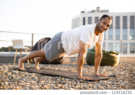 Strong male in plank position on mat during sunrise against urban background. 114518230