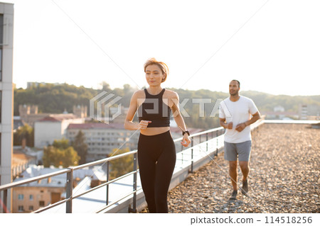 Young sporty woman in black top running in morning with male partner. Young sporty woman in black top running in morning with male partner. 114518256