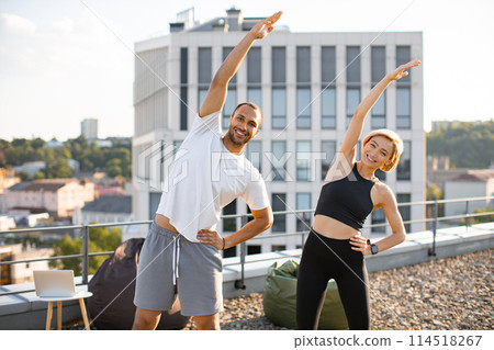 Sports couple making health gymnastics in morning on roof terrace of building. 114518267