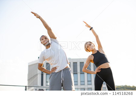 Sports couple making health gymnastics in morning on roof terrace of building. Sports couple making health gymnastics in morning on roof terrace of building. 114518268