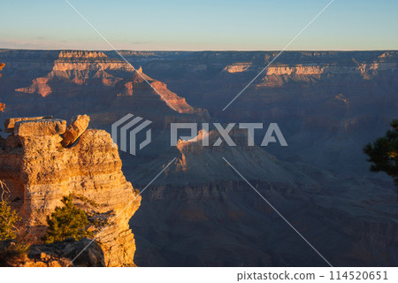 Breathtaking view of Grand Canyon at sunrise or sunset. Intricate layers showcase rugged terrain under warm light. Clear blue sky. Located in Arizona, USA. Breathtaking view of Grand Canyon at sunrise or sunset. Intricate layers showcase rugged terrain under warm light. Clear blue sky. Located in Arizona, USA. 114520651