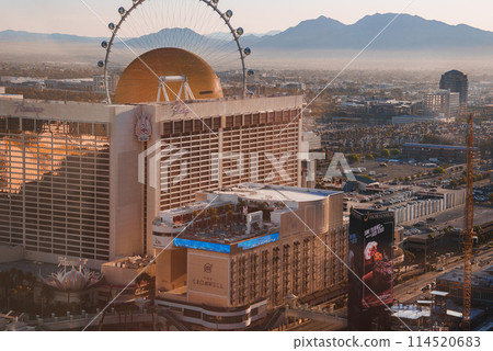 Las Vegas Strip view at sunset with a large hotel casino and prominent Ferris wheel in the background. Vibrant scene with mountain silhouettes and golden hour lighting. Las Vegas Strip view at sunset with a large hotel casino and prominent Ferris wheel in the background. Vibrant scene with mountain silhouettes and golden hour lighting. 114520683