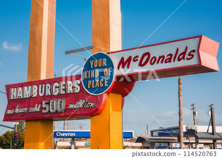 Vintage McDonald's sign featuring large golden arches, red HAMBURGERS, and over 500 million sold text. Americana vibe with palm tree and blue sky in urban setting, likely Los Angeles, California. 114520763