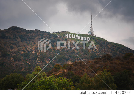 Iconic Hollywood Sign on Mount Lee in the Hollywood Hills area of the Santa Monica Mountains. White letters against a backdrop of greenery under a cloudy sky in Los Angeles. Iconic Hollywood Sign on Mount Lee in the Hollywood Hills area of the Santa Monica Mountains. White letters against a backdrop of greenery under a cloudy sky in Los Angeles. 114520764