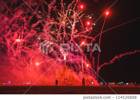 Vibrant night scene at desert music and art festival, possibly Burning Man in Black Rock Desert, Nevada. Silhouettes, fireworks, burning structure, surreal atmosphere, desert horizon. Vibrant night scene at desert music and art festival, possibly Burning Man in Black Rock Desert, Nevada. Silhouettes, fireworks, burning structure, surreal atmosphere, desert horizon. 114520898