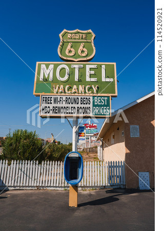 Vintage Route 66 motel sign in Barstow, USA. Weathered, vibrant colors, retro design. Nostalgic scene with payphone booth, picket fence, and commercial signs. 114520921