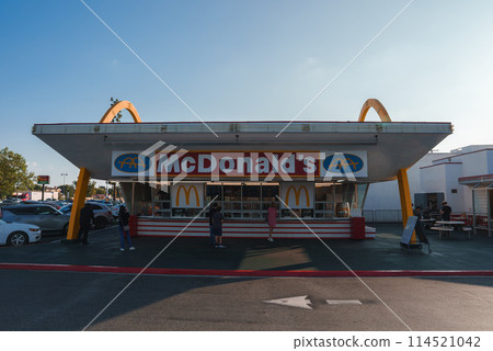 Iconic McDonald's restaurant featuring retro design with golden arches and red white color scheme. Clear sky and cars parked. Location may be in Los Angeles. Iconic McDonald's restaurant featuring retro design with golden arches and red white color scheme. Clear sky and cars parked. Location may be in Los Angeles. 114521042