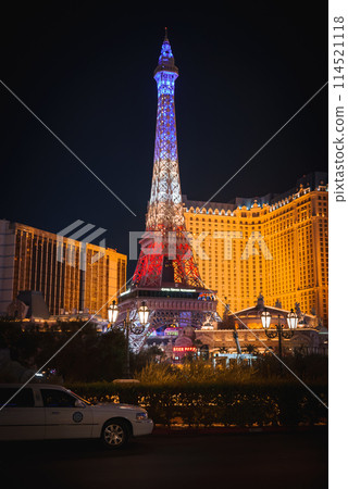 Vibrant Las Vegas Strip night scene white security vehicle, Eiffel Tower replica, lush greenery, opulent hotels glowing with lights. Captures city's lively essence. 114521118
