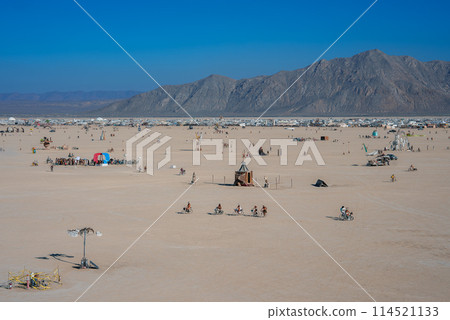 Explore a vast desert scene with art installations and festival attendees. A breathtaking landscape with mountains in the backdrop, perfect for creative events. 114521133