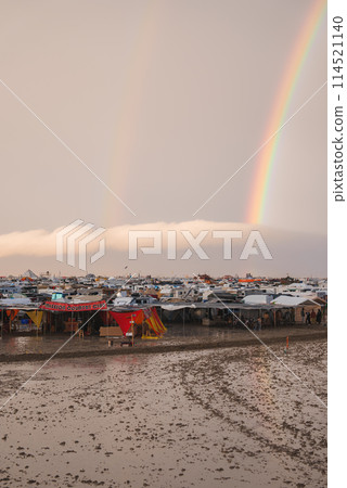 Explore a vibrant desert settlement with RVs, tents, and a rainbow canopy over MISSION COUNTRY CLUB. Muddy ground hints at recent rain in this temporary festival community. 114521140