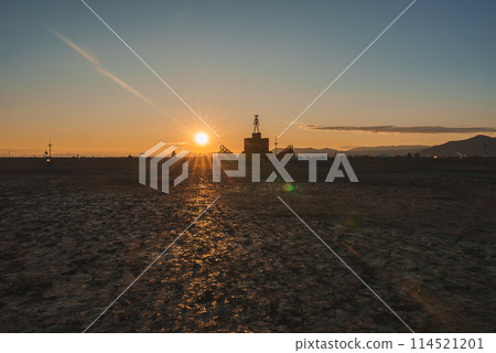 Serene desert landscape at sunset with warm golden glow, silhouetted structure, distant mountains, and festival vibes. Location unspecified, possible remote desert setting. 114521201