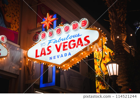 Iconic Welcome to Fabulous Las Vegas Nevada sign lights up at night, symbolizing city's glamor. Palm trees and vibrant lights adorn the nocturnal scene of the famous Las Vegas Strip. Iconic Welcome to Fabulous Las Vegas Nevada sign lights up at night, symbolizing city's glamor. Palm trees and vibrant lights adorn the nocturnal scene of the famous Las Vegas Strip. 114521244