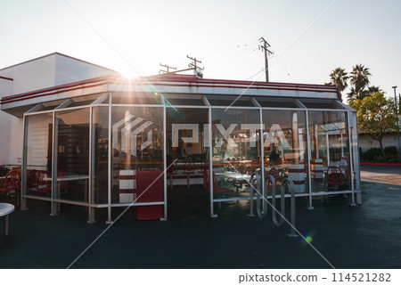 Classic American diner in Los Angeles with mid 20th century style, white exterior, red trim, traditional booth seating, and outdoor area with red and white chairs under a canopy. Classic American diner in Los Angeles with mid 20th century style, white exterior, red trim, traditional booth seating, and outdoor area with red and white chairs under a canopy. 114521282