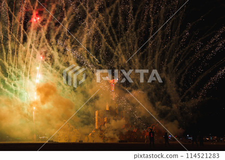 Vibrant scene at a music and art festival in a desert with spectators as silhouettes, fireworks in green and gold, and a large glowing structure in the center. Location hints at Burning Man. Vibrant scene at a music and art festival in a desert with spectators as silhouettes, fireworks in green and gold, and a large glowing structure in the center. Location hints at Burning Man. 114521283