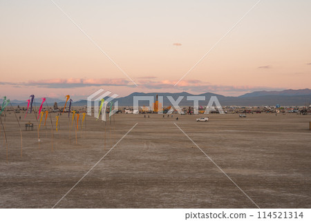 Desert landscape at sunrise or sunset with soft pastel skies, mountain range, colorful art installations, and festival structures in the background. Tranquil atmosphere, location unspecified. Desert landscape at sunrise or sunset with soft pastel skies, mountain range, colorful art installations, and festival structures in the background. Tranquil atmosphere, location unspecified. 114521314