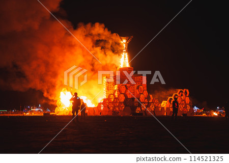 Vibrant desert festival night scene with a fiery spectacle and attendees gazing at a massive structure ablaze, creating a striking contrast of colors. Vibrant desert festival night scene with a fiery spectacle and attendees gazing at a massive structure ablaze, creating a striking contrast of colors. 114521325