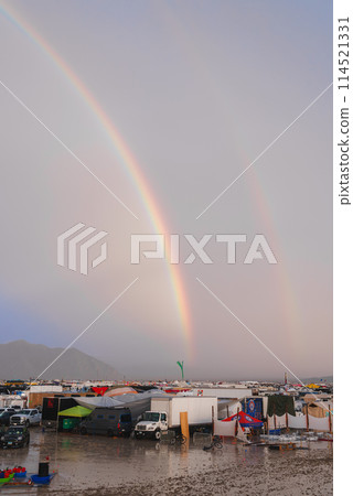 Vibrant double rainbow over desert music and art festival grounds with tents, vehicles, and art installations after rare rainfall creating a scenic backdrop. 114521331