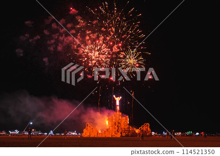 Vibrant night scene at a desert music and art festival with a wooden structure ablaze and fireworks lighting up the sky, capturing a sense of communal celebration. Vibrant night scene at a desert music and art festival with a wooden structure ablaze and fireworks lighting up the sky, capturing a sense of communal celebration. 114521350