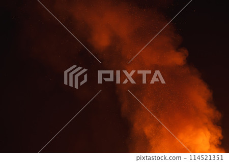Dynamic scene of large fire at night in a desert setting. Bright orange flames contrast with dark smoke, creating a striking visual display in the dark sky. 114521351