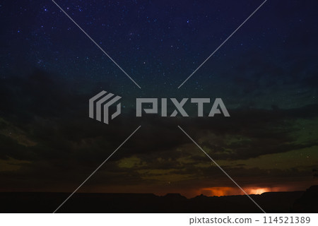 Serene night sky with numerous bright stars over a canyon or desert landscape. Dramatic contrast with clouds and distant glow at the Grand Canyon. Serene night sky with numerous bright stars over a canyon or desert landscape. Dramatic contrast with clouds and distant glow at the Grand Canyon. 114521389