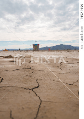 Desert landscape with cracked, dry earth in foreground, colorful tower in the background. Remote location, unique festival vibe. Expansive sky, mountains. Desert landscape with cracked, dry earth in foreground, colorful tower in the background. Remote location, unique festival vibe. Expansive sky, mountains. 114521459