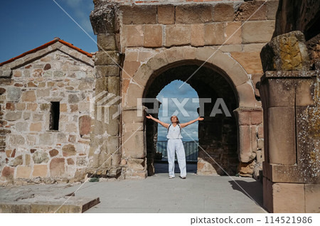 Happy senior traveler woman tourist posing outdoors in ancient Europe fortress ruins. Mature female arms outstretched. Retired old people summer holiday vacation, active lifestyle freedom concept. 114521986