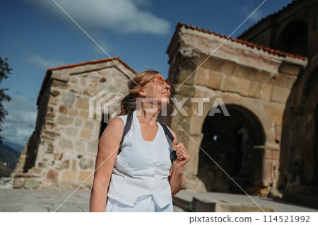 Elderly smiling senior traveling woman backpacker tourist walking posing outdoors in ancient Europe fortress ruins. Retired mature people summer holiday vacation, active lifestyle concept. 114521992