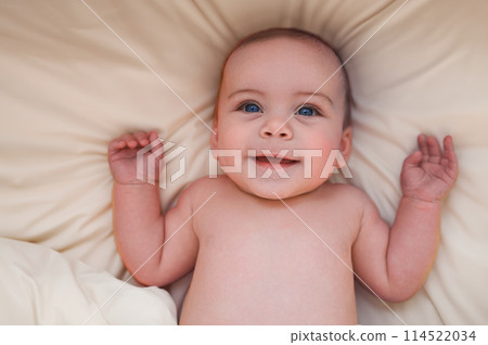 Cute emotional funny smiling newborn little boy laying on beige sheets in bed or crib. Baby goods packaging template. Healthy child, concept of hospital and happy motherhood. Infant baby. Nursery 114522034