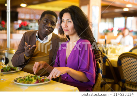 Cheerful african american man flirting with asian woman in restaurant Cheerful african american man flirting with asian woman in restaurant 114523134