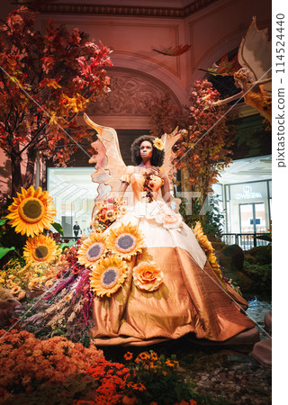 Experience the opulence of a luxurious indoor setting in Las Vegas. Admire a golden figure with floral costume and wings, surrounded by a garden of warm hues. 114524440
