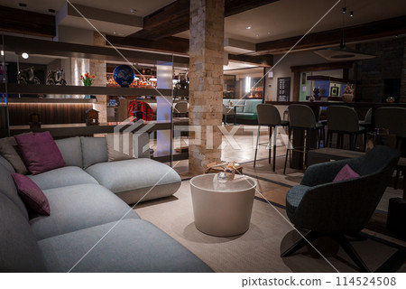 Sophisticated lounge area in luxury hotel in Zermatt, Switzerland. Modern design with cozy elements. Plush sofa, coffee table, bar, ambient lighting, elegant decor. Sophisticated lounge area in luxury hotel in Zermatt, Switzerland. Modern design with cozy elements. Plush sofa, coffee table, bar, ambient lighting, elegant decor. 114524508