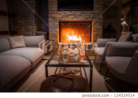 Inviting lounge area in luxury Zermatt hotel with roaring fireplace, modern seating, and cozy atmosphere. Ideal for relaxation and comfort in Switzerland. 114524514