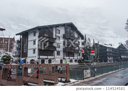 Alpine street view in Zermatt, Switzerland featuring a snowy scene with a building, wooden fence, and no entry sign. Tranquil winter atmosphere captured in this image. 114524581