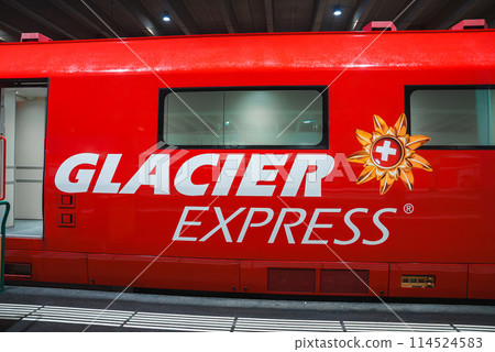 Close up view of a red train carriage with GLACIER EXPRESS logo and Swiss flag flower emblem. Modern, stationary train at Swiss Alps, Zermatt station. 114524583