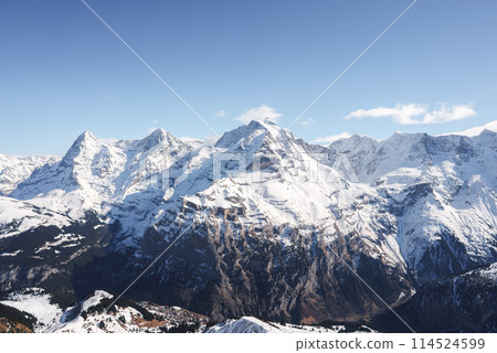 Experience the awe inspiring Swiss Alps with snow covered peaks and rugged slopes captured from the Murren ski resort. Majestic mountains under a clear blue sky create a dramatic alpine scene. 114524599