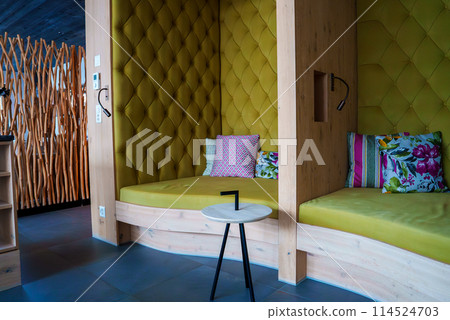 Modern, stylish interior with vibrant chartreuse tufted wall, colorful throw pillows on bed, sleek round table, and unique wooden screen or partition. Dark gray tile floor, ambient lighting. Modern, stylish interior with vibrant chartreuse tufted wall, colorful throw pillows on bed, sleek round table, and unique wooden screen or partition. Dark gray tile floor, ambient lighting. 114524703