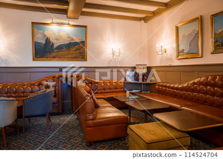 Elegant lounge with luxury furnishings classic design, leather sofa, mountain paintings, tufted armchairs, traditional carpet, warm lighting, refined decor. Elegant lounge with luxury furnishings classic design, leather sofa, mountain paintings, tufted armchairs, traditional carpet, warm lighting, refined decor. 114524704