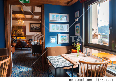 Interior of a cozy, elegantly decorated dining area in a restaurant or hotel. Warm atmosphere, mix of traditional and contemporary design. Mountain view in the background. 114524723