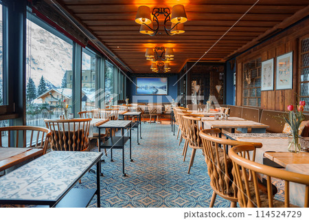 Interior of a cozy dining area in a rustic restaurant or cafe with wooden decor, elegant carpeting, and mountain views. Tranquil and inviting ambiance. Interior of a cozy dining area in a rustic restaurant or cafe with wooden decor, elegant carpeting, and mountain views. Tranquil and inviting ambiance. 114524729