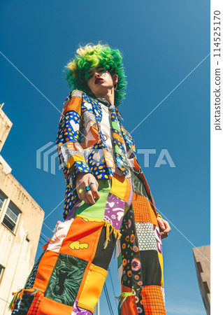 A man with green hair and a multicolored outfit poses for a photo 114525170