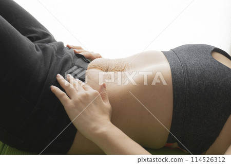 A woman lying on her back on a yoga mat with stretch marks remaining on her stomach after giving birth 114526312