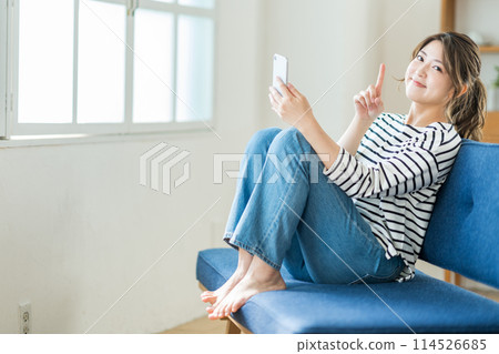A young woman who operates a smartphone in the living room. 114526685